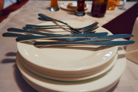 clean dishes are stacked with cutlery lying on topの写真素材