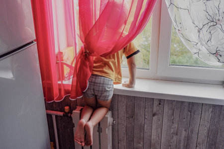 a little boy climbed with his feet on the radiator to look out the window.の写真素材