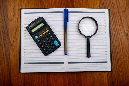 a magnifying glass, a pen, a calculator and a diary are on the table.financial planning.a concept for planning monthly expensesの写真素材