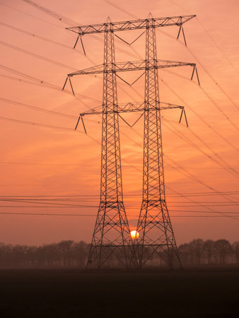 Silhouette of a power transmission tower at sunset background with a very low sun.