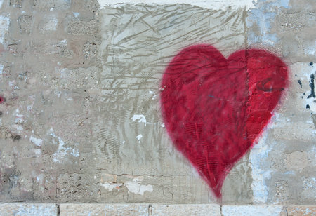 Red heart painted on the right side of a concrete old scratched grunge grey wall. A piece of a brick wall below. Copy space for text or images on the left hand sideの写真素材