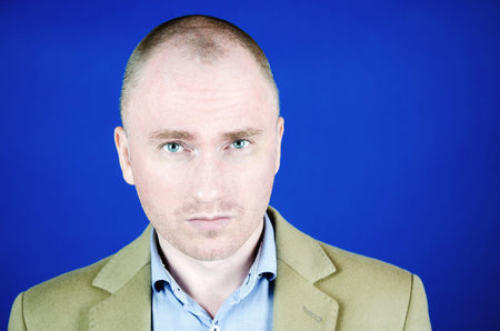 Portrait of a young man. The gaze of a handsome man in a cream coat with copy space. Blue background