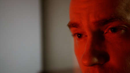 A young man with a serious look. Frowning man in red tones evil smileの写真素材
