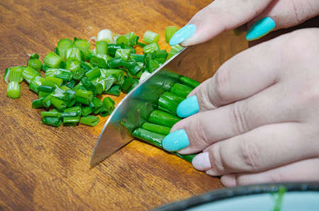 Female hands with a knife, slicing vegetables on a wooden board on a white background. woman cuts green onionsの写真素材