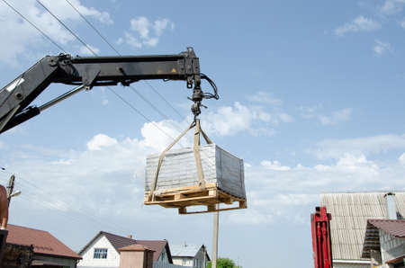 A man of a European race helps with loading tiles to the ground from a car. Delivery and unloading of building materials to the house. Truck crane unloaded street tiles.の写真素材