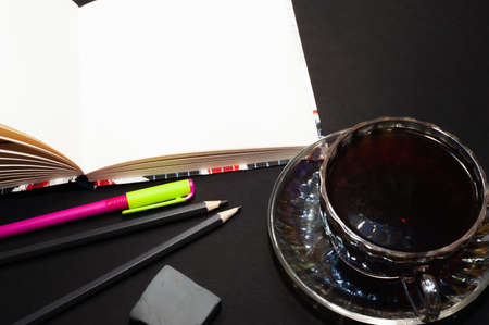 Top view of a cup of coffee and a notebook with pencils and an eraser, isolate on blackの写真素材