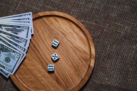 three dice laying over a pile of money on a wooden plate gameの写真素材