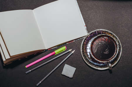 Top view of a cup of coffee and a notebook with pencils and an eraser, isolate on blackの写真素材