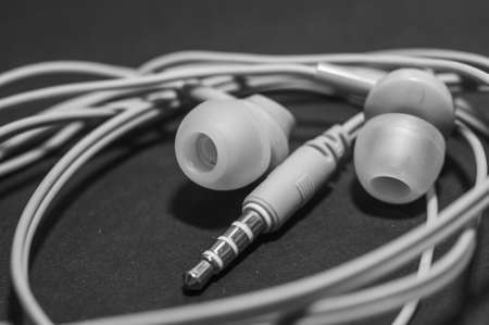 White twisted wired headphones on a monochromatic black surface, close-up. Headset for a mobile phone. musicの写真素材
