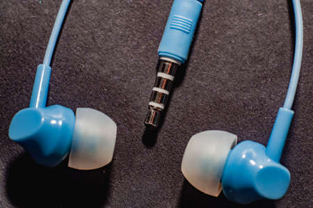 Blue twisted wired headphones on a monochromatic black surface, close-up. Headset for a mobile phone.の写真素材