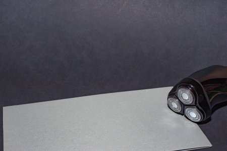 Glossy black electric razor for men on a black background and a gray envelope backing.
