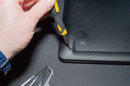 Hands of a computer repairman removing the back cover of the notebook.Computer repair shop. Engineer performing laptop maintenance. Hardware developer fixing electronic components. PC technologyの写真素材