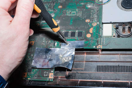 Hands of a computer repairman removing the back cover of the notebook.Computer repair shop. Engineer performing laptop maintenance. Hardware developer fixing electronic components. PC technologyの写真素材