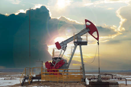 Crude oil pump jack at oilfield on sunset backround. Fossil crude output and fuels oil production. Oil drill rig and drilling derrick.の写真素材