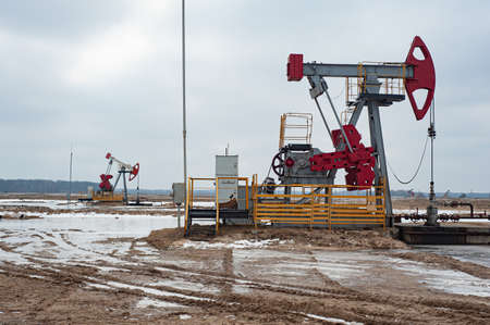 Crude oil pump jack at oilfield on sunset backround. Fossil crude output and fuels oil production. Oil drill rig and drilling derrick.の写真素材
