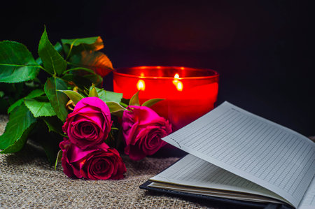 A red rose with a book and a burning candle on a black background. From above of burning candle with fresh red with a rose on book on black backgroundの写真素材