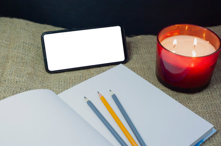 A phone with a clean, free space, a notebook and candles in a red glass, ideas for recreation, planning, prospectsの写真素材