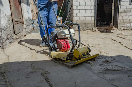 Worker in uniform and knee pads use vibratory plate compactor for path construction.の写真素材