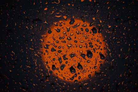 Water drops on a window glass after the rain. The sun and sky with clouds on background. Sunset outside window during raining. Bright texture of water dropsの写真素材