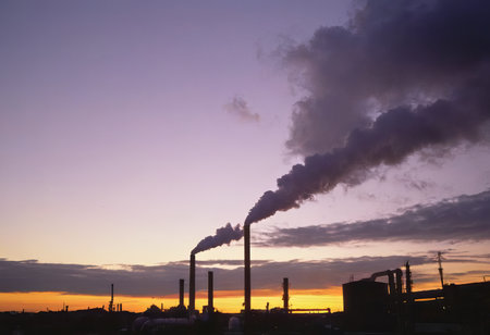 Smoke from heating station in big city during winter season at sunset. Smokestack pipes emitting co2 from coal thermal power plant into atmosphere. Air pollution and emission ecology problem conceptの素材