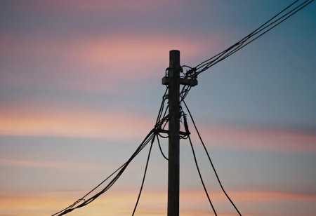 A neatly arranged row of telephone poles stands tall against the stunning backdrop of a vibrant sunset, creating a beautiful sceneの素材
