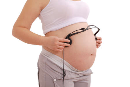 Pregnant woman with headphones on her stomach on white backgroundの写真素材