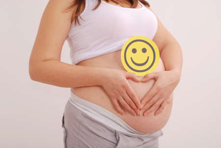 Pregnant woman clasped her hands in the shape of a heart on grey backgroundの写真素材