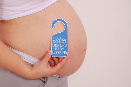 Do Not Disturb Baby Sleeping sign in his hands pregnant woman on grey background