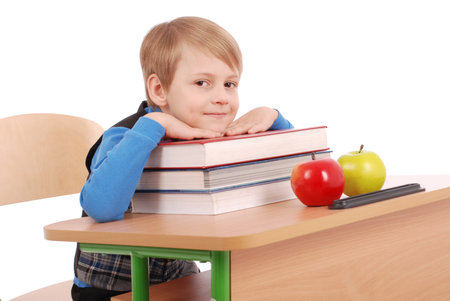 Boy sitting at a school desk isolated on white