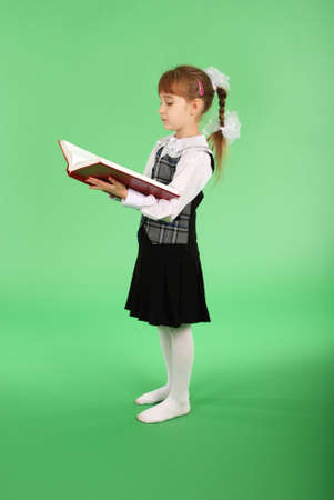 Girl in school uniform reading a book isolated on greenの写真素材