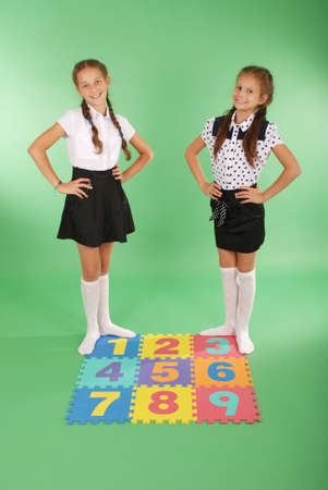 Two girls on rug with numbers one, two, three, four, five, six, seven, eight, nine on green backgroundの写真素材