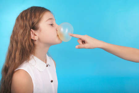 Two young girls playing with chewing gum isolated on blueの写真素材