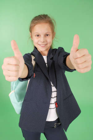 Smiling young school girl showing thumbs up isolated on green backgroundの写真素材