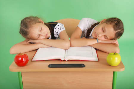 Two school girls sleeping on a stack of books at her desk isolated on greenの写真素材