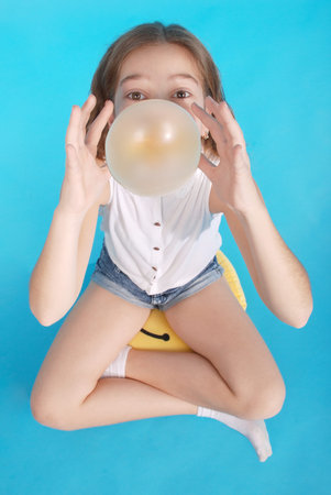 Top view of beautiful young brunette  girl blowing bubble gum isolated on blueの写真素材