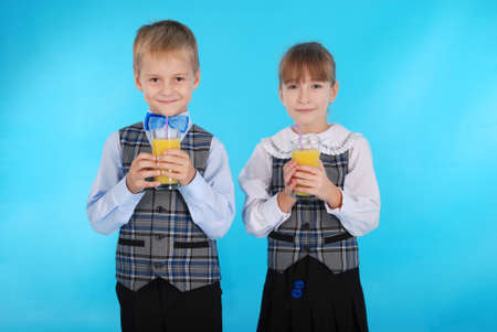Girl and boy in school uniform drink juice - healthy diet. Photos on a blue backgroundの写真素材