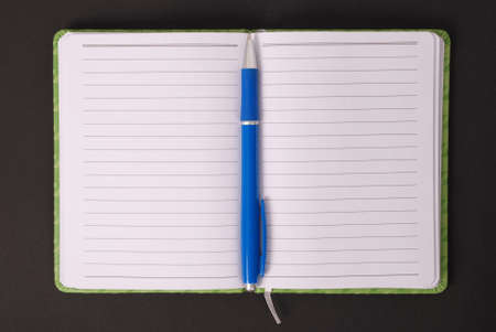 Green open notebook with blue pen isolated on black background red soft shadowの写真素材