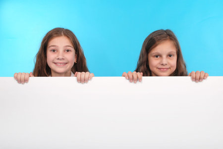 Two happy smiling beautiful young girl showing blank signboard or copyspace for slogan or text,...