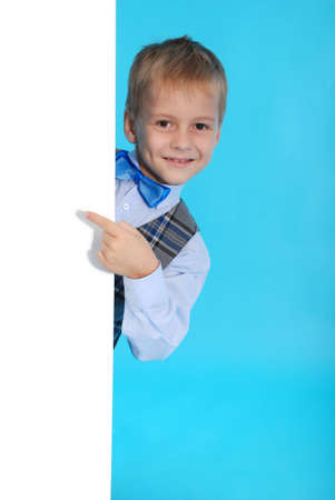 A smiling schoolboy posing behind a white billboard isolated on blue backgroundの写真素材