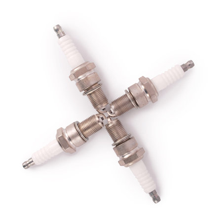 Four new spark plugs on a white background with soft shadow