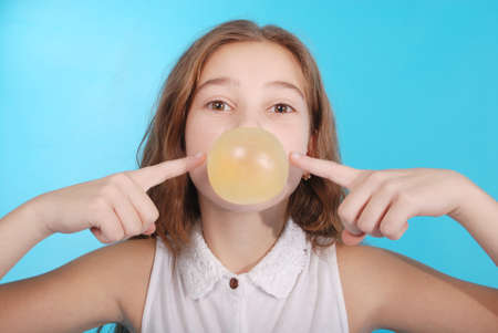 Girl blowing a big bubble gum bubble isolated on blueの写真素材