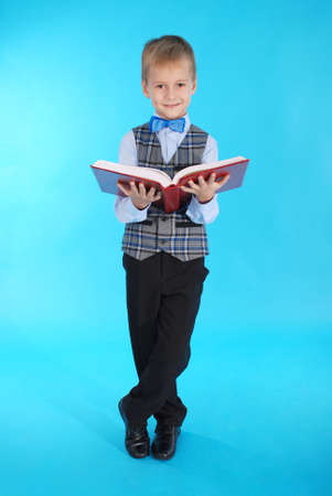 Boy in school uniform holding an open red book on a blue backgroundの写真素材