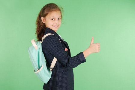 Smiling young school girl showing thumbs up isolated on green backgroundの写真素材