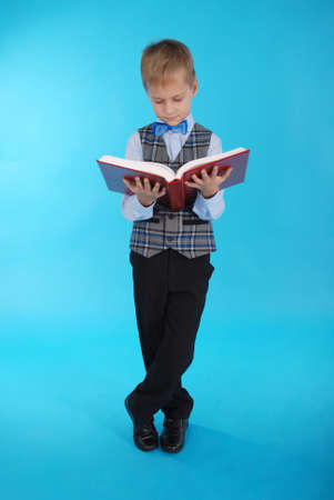 Boy in school uniform reading open book on a blue backgroundの写真素材