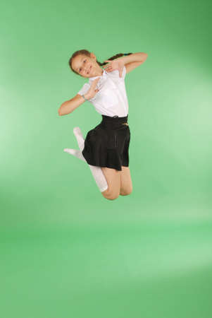 Cute happy school girl jumping. Isolated green background. Happiness, friendship, fashionable concept.の写真素材