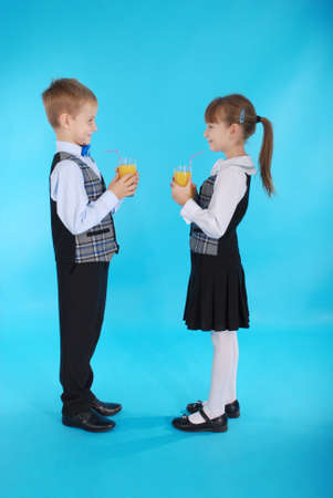 Girl and boy in school uniform drink juice - healthy diet. Photos on a blue backgroundの写真素材