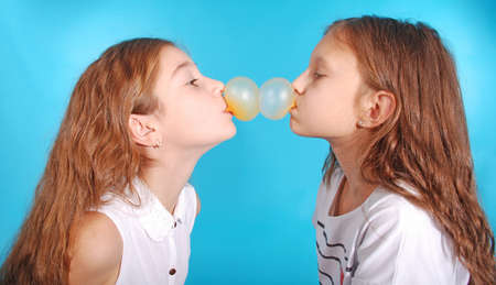 Two young girls playing with chewing gum isolated on blueの写真素材