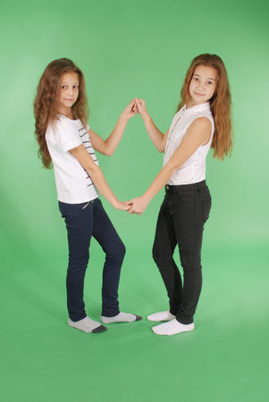 Young school girls holding hands and smiling at camera. Studio shot on green background.の写真素材