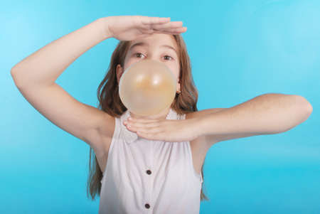 Girl blowing a big bubble gum bubble isolated on blueの写真素材