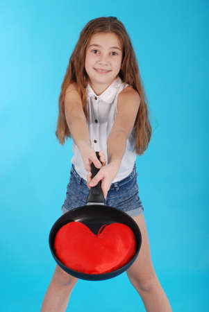 Young girl with a frying pan isolated on blue backgroundの写真素材